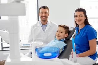 A young boy sits in a dental chair, flanked by his concerned mother and father, preparing for a medical procedure.