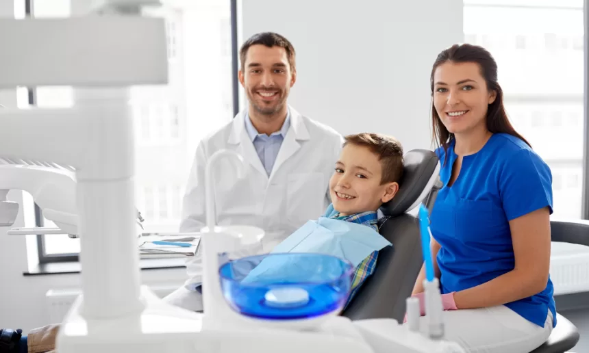 A young boy sits in a dental chair, flanked by his concerned mother and father, preparing for a medical procedure.