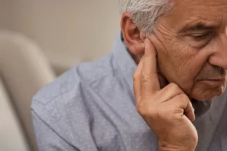 An older man examines his ear, reflecting on the process of ear reconstruction and its impact on his life.