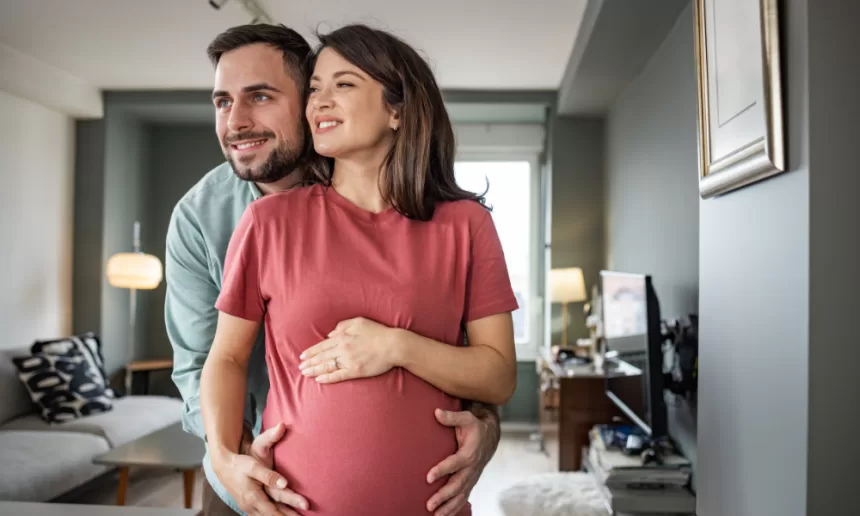 A pregnant woman and man stand together in a cozy living room, symbolizing hope and family after fertility surgery.