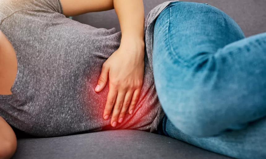 A woman sitting on a couch, visibly in discomfort, reflecting on her recovery after fibroid removal surgery.