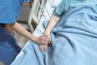 A compassionate nurse gently holds a patient's hand in a hospital bed, providing comfort during hand surgery recovery.