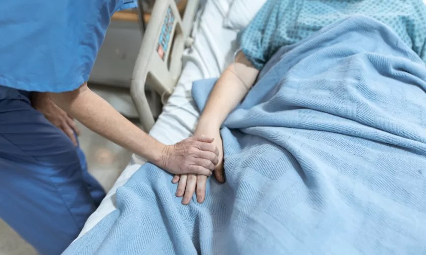 A compassionate nurse gently holds a patient's hand in a hospital bed, providing comfort during hand surgery recovery.