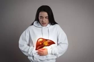 A woman in a white sweatshirt gently holds her stomach, reflecting on her journey after liver cancer surgery.