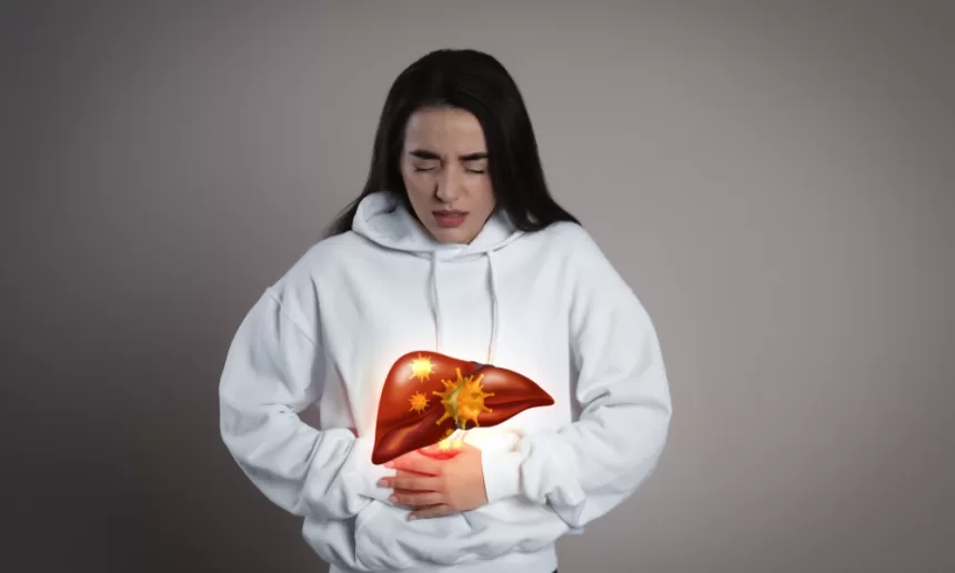 A woman in a white sweatshirt gently holds her stomach, reflecting on her journey after liver cancer surgery.