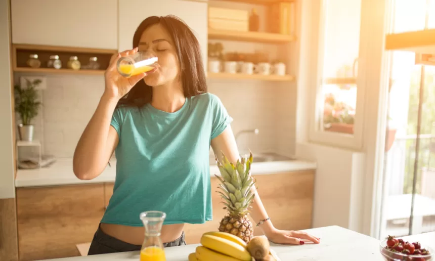 A woman enjoying a refreshing glass of orange juice, symbolizing a healthy morning routine.