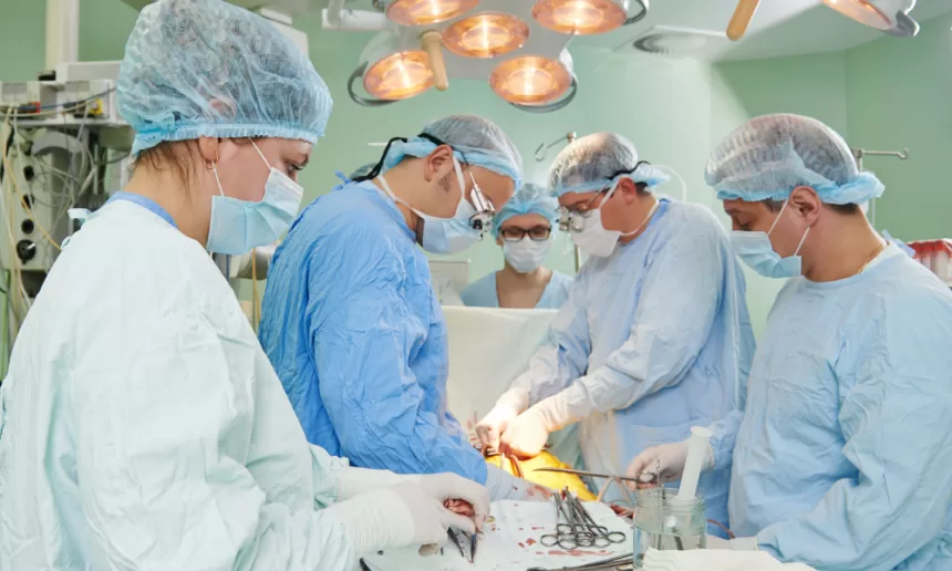A team of medical professionals in surgical attire performing pediatric cardiac surgery on a patient.