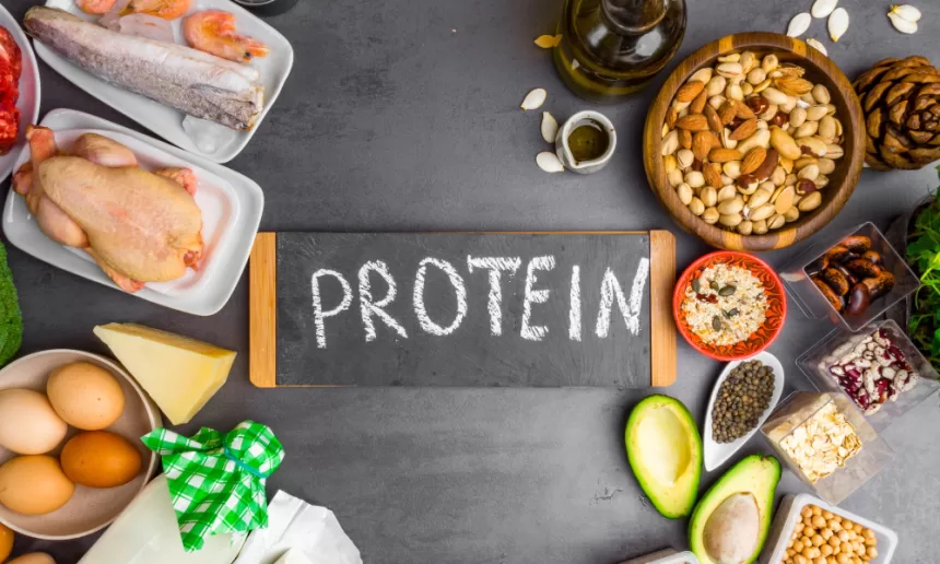 Collagen protein powder in a scoop, surrounded by healthy food sources like fish, eggs, and leafy greens, on a wooden table.