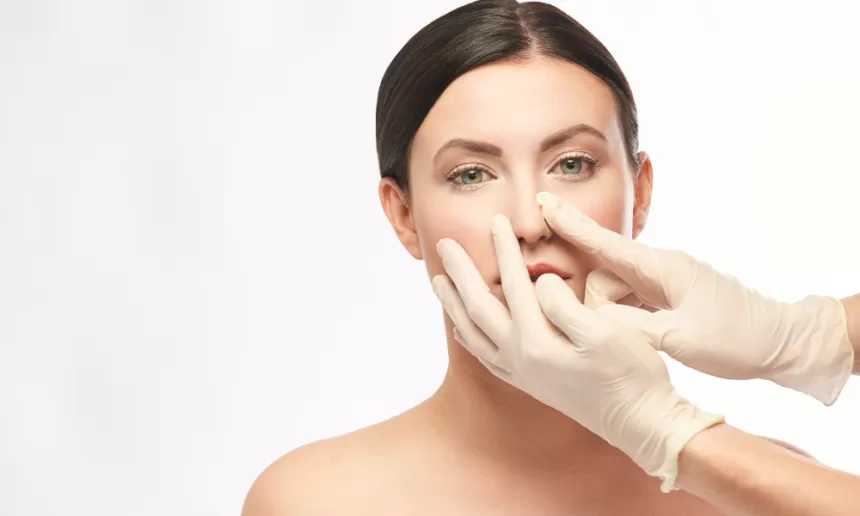 A woman undergoing rhinoplasty surgery as a doctor carefully performs the nose reshaping procedure.