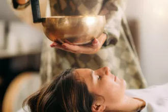 A woman enjoys a sound healing therapy massage, holding a bowl, promoting relaxation and wellness.