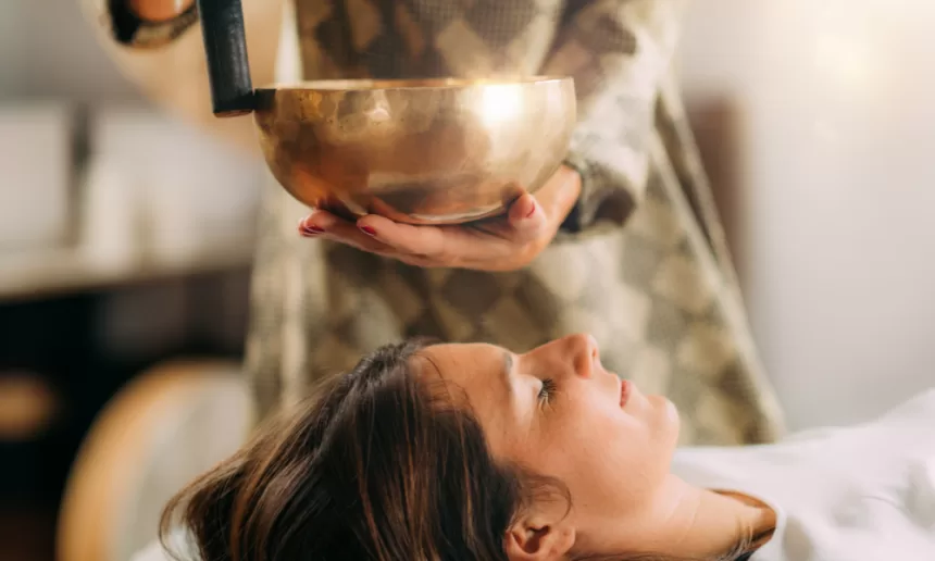 A woman enjoys a sound healing therapy massage, holding a bowl, promoting relaxation and wellness.