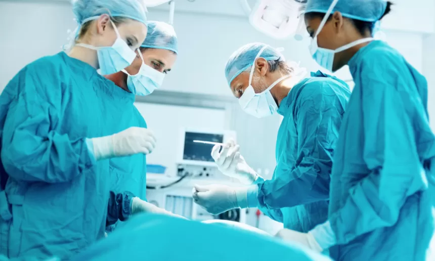 Surgeons in blue scrubs perform pancreas surgery in a sterile operating room, focused on the intricate procedure.