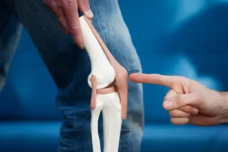A person points at their knee joint, illustrating the area affected by total knee replacement surgery.