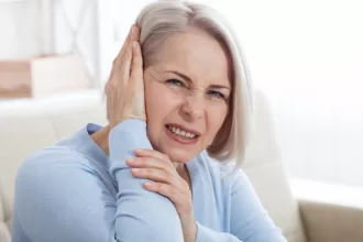 A woman holding her head in pain, experiencing a headache and earache, highlighting the impact of Trigeminal Neuralgia Surgery.