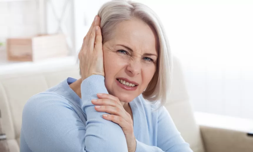 A woman holding her head in pain, experiencing a headache and earache, highlighting the impact of Trigeminal Neuralgia Surgery.