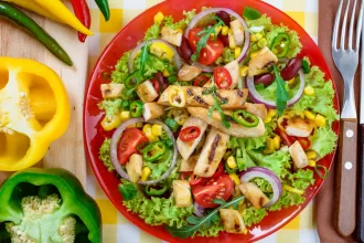 Rainbow plates of vegan-keto food, featuring avocado, nuts, seeds, leafy vegetables and coconut oil laid out neatly on a rough wooden table.