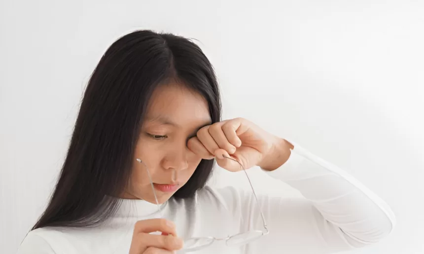 A woman with a concerned expression holds her head while looking at her phone, reflecting on her diabetic retinopathy surgery.
