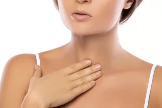 A woman gently holds her neck, reflecting on her recent vocal cord surgery for nodules and polyps.